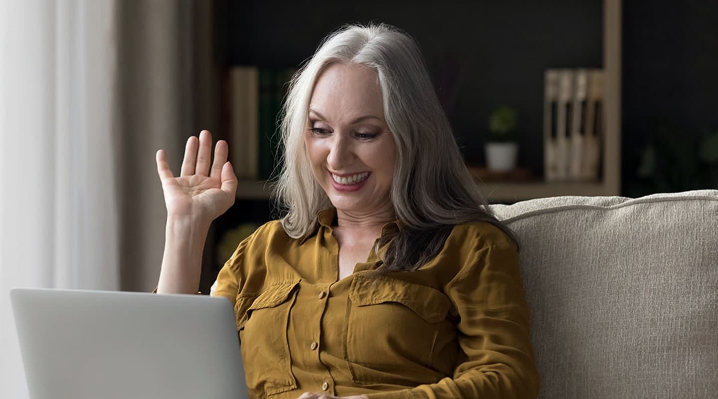 woman smiles at her laptop during a telehealth appointment