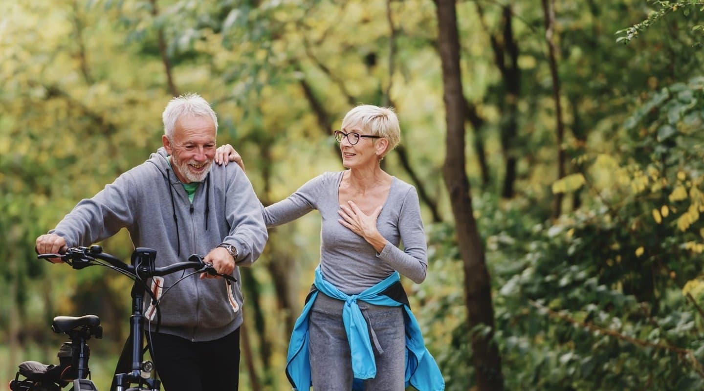 Couple walking through the woods with a bike.