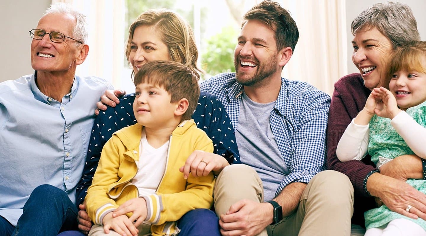 a multigenerational family sits on a couch and smiles for a picture