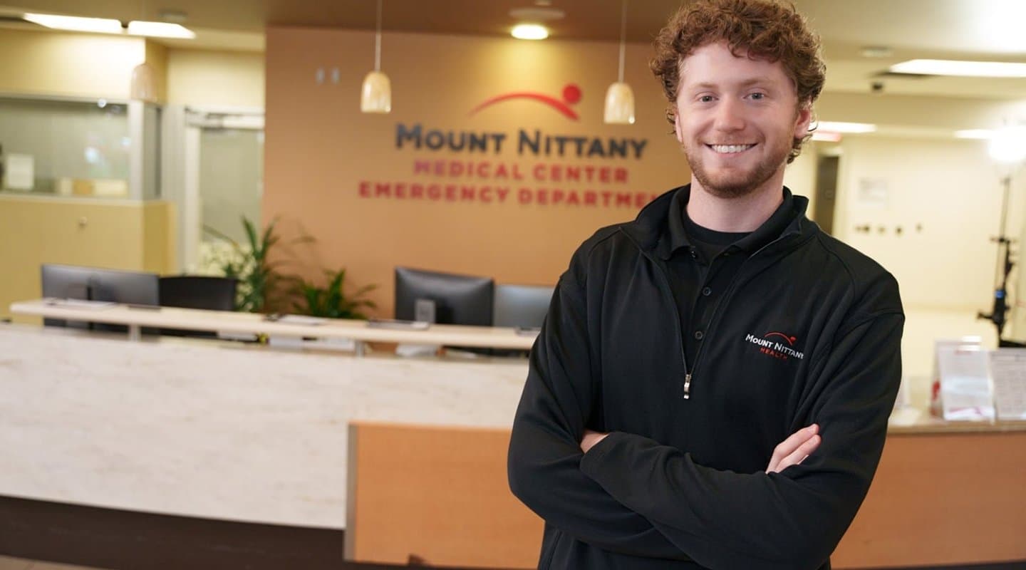 Smiling Mount Nittany Health Employee stands in front of reception desk.