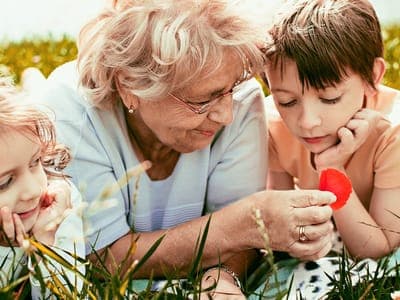 grandmother and grandkids sit in the grass and look at flowers
