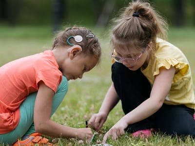 two young girls play outside and one wearings a hear device on her ear