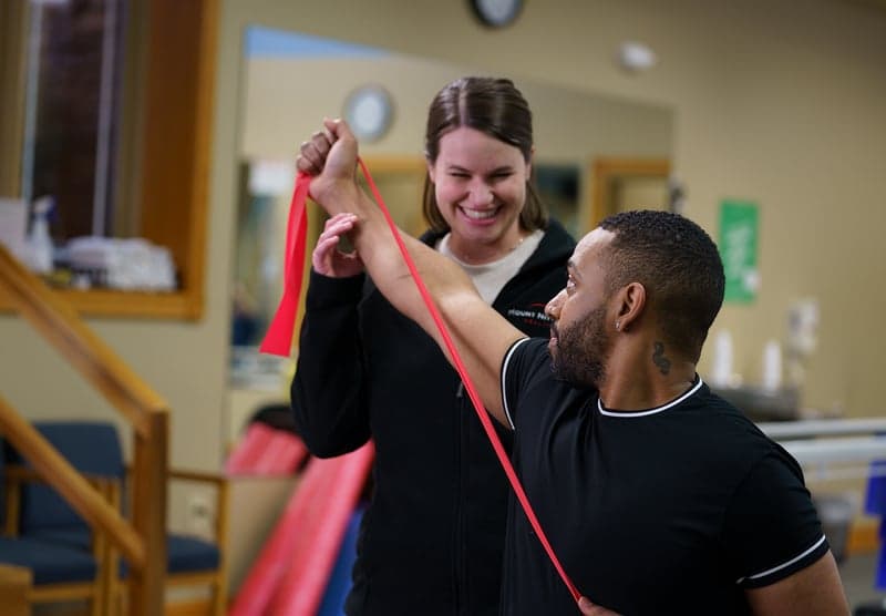 Zoe Carr helps a male patient stretch using resistance bands