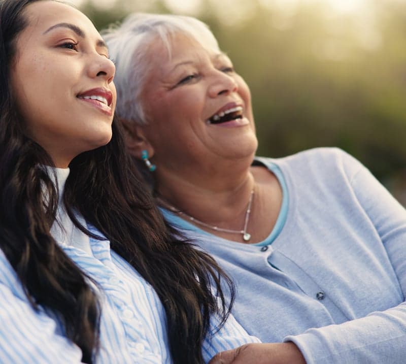 mom and adult daughter sit outside and laugh