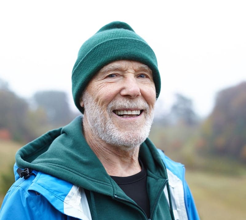 An older man wearing a green beanie and hoodie stands outside