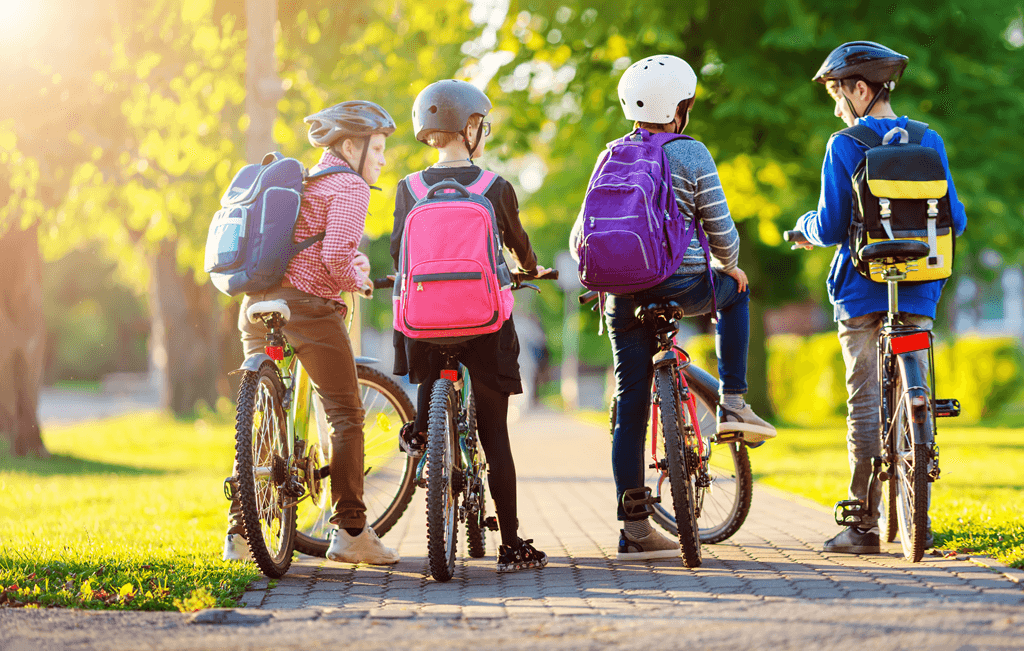 Children with rucksacks riding on bikes in the park near school