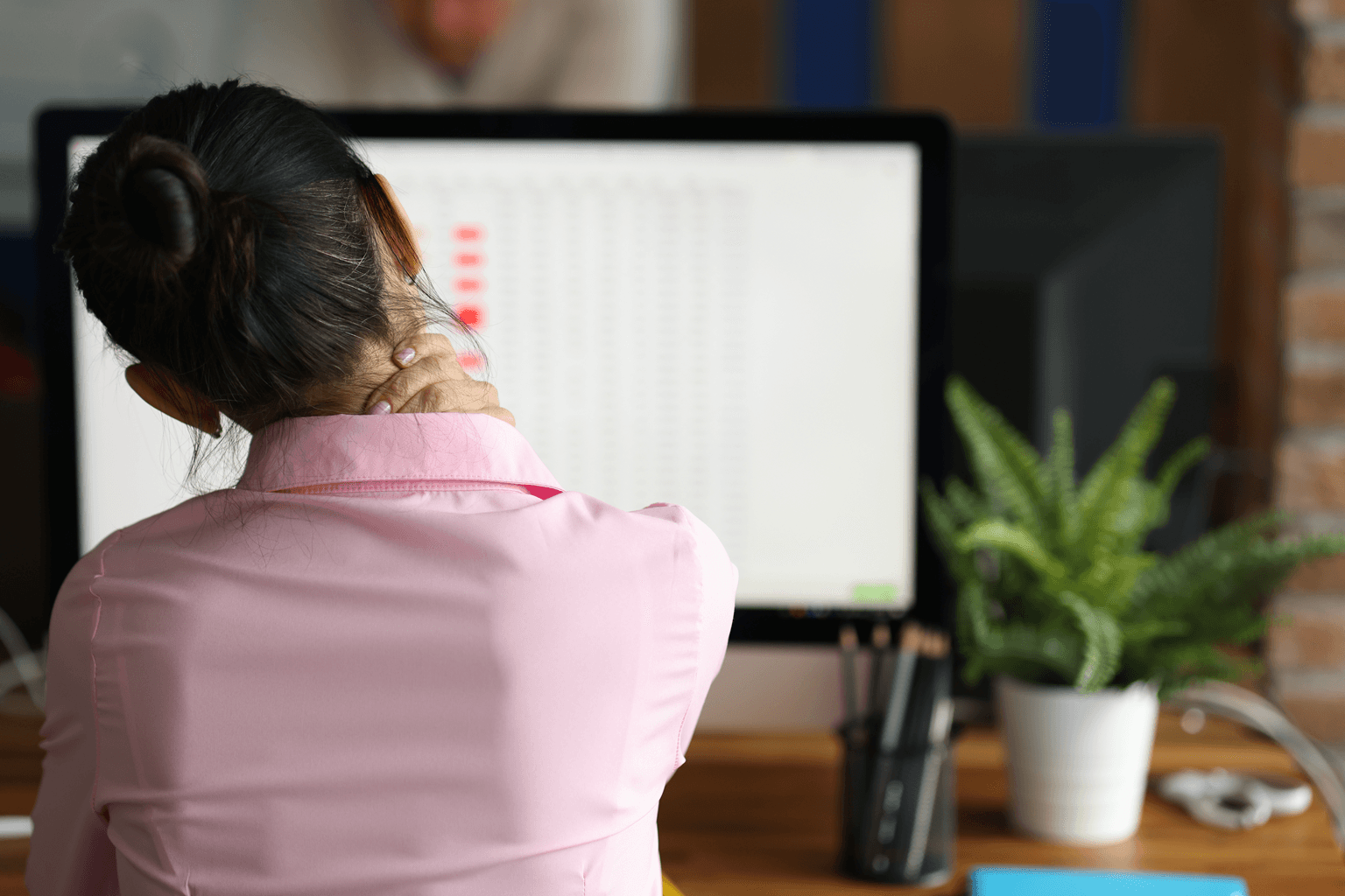 woman sits at computer and massages pain in her neck