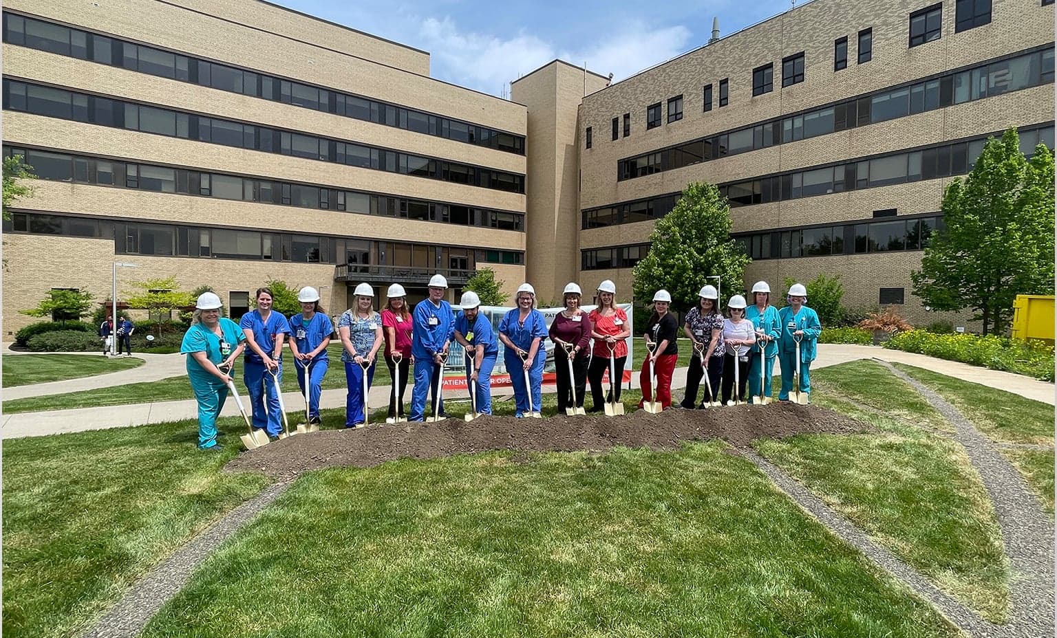 Employees gather for the groundbreaking and stand with shovels in the dirt