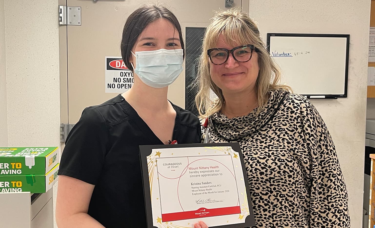 Kristina Sanders wears and mask and holds her employee of the month certificate while standing next to Tiffany Cabibbo, CNO