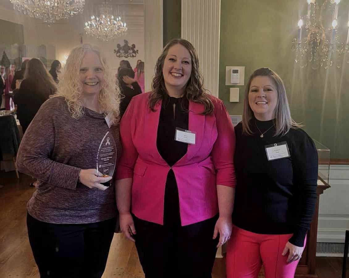 Three women pose with glass award