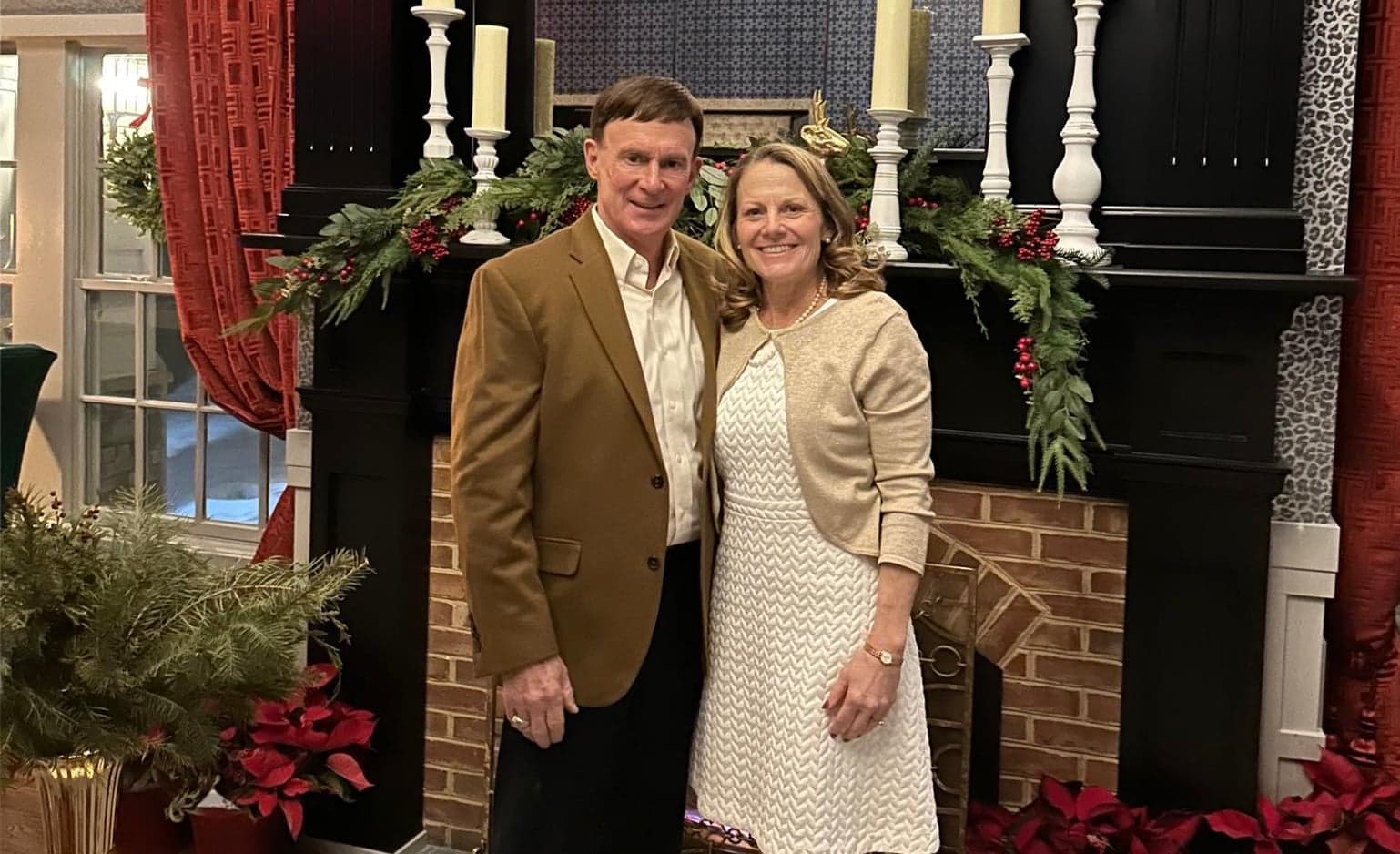 Jack and Karen Infield pose in front of a brick fireplace with holiday decorations