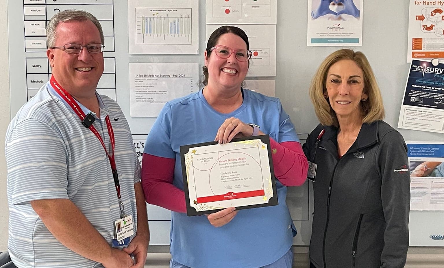 Kim Ross, RN holds her Employee of the Month certificate and poses with Rick Slebodnik, RN and Kathleen Rhine in front of a bulletin board