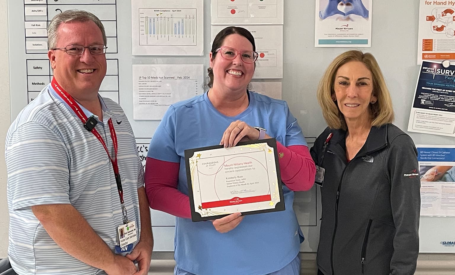Kim Ross, RN holds her Employee of the Month certificate and poses with Rick Slebodnik, RN and Kathleen Rhine in front of a bulletin board