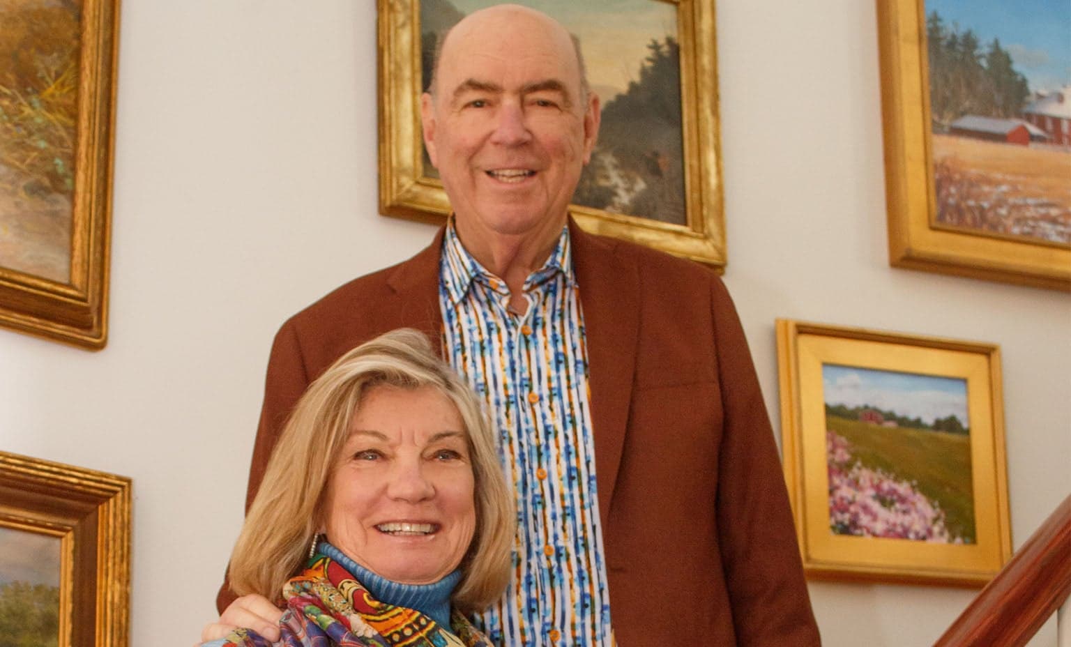 Bill and Connie Hayes pose on their staircase in front of frame paintings