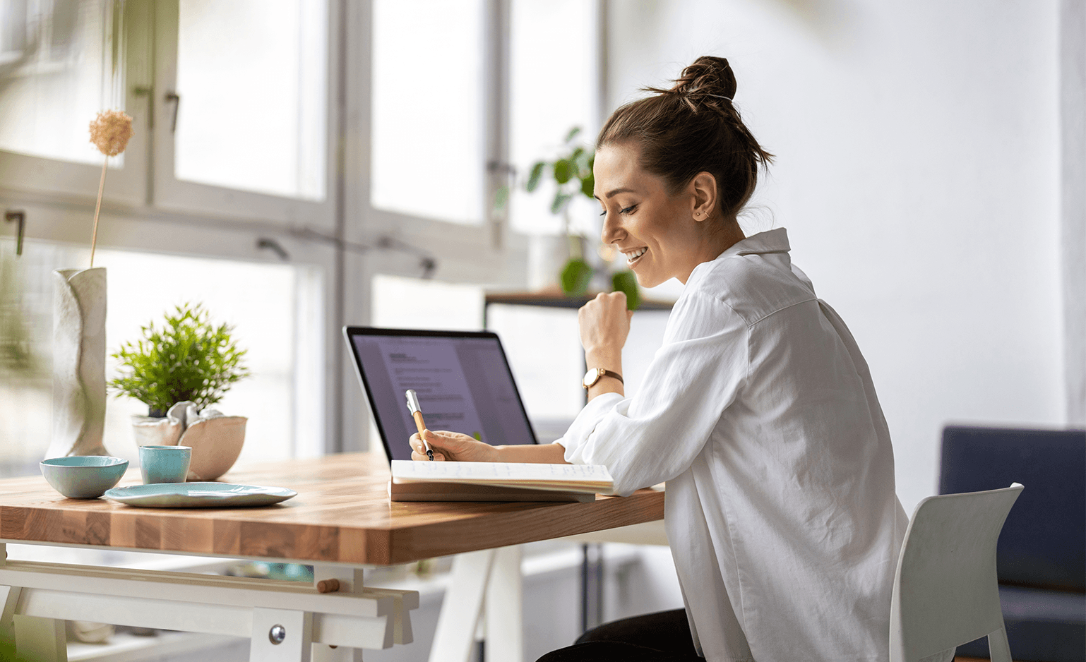 woman at desk working on computer and writing in notebook