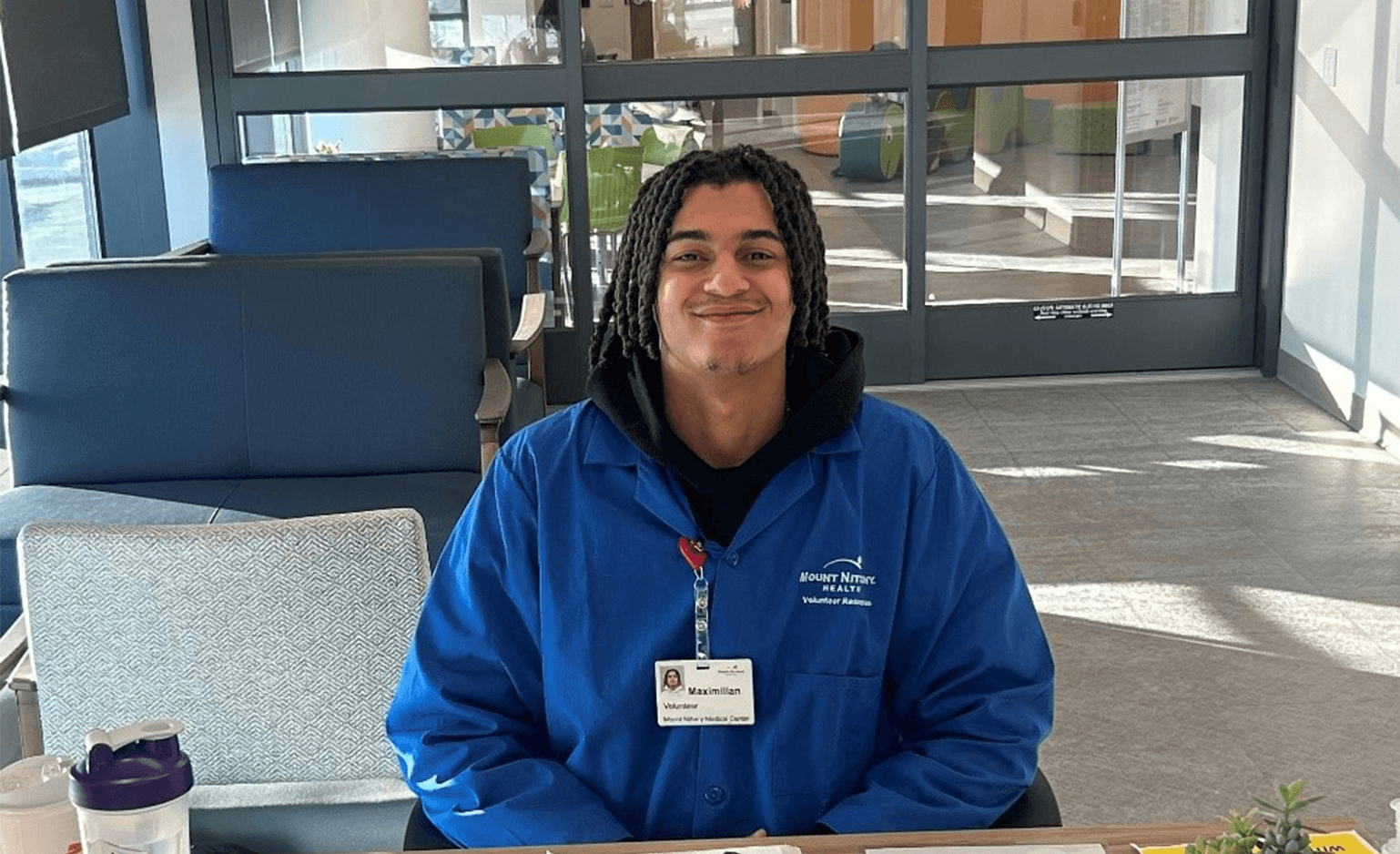 Mount Nittany Health volunteer Maximilian Croke sitting behind welcome desk, smiling.