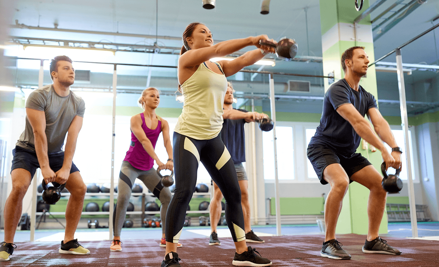 group of 5 men and women exercising in a gym, swinging kettle balls