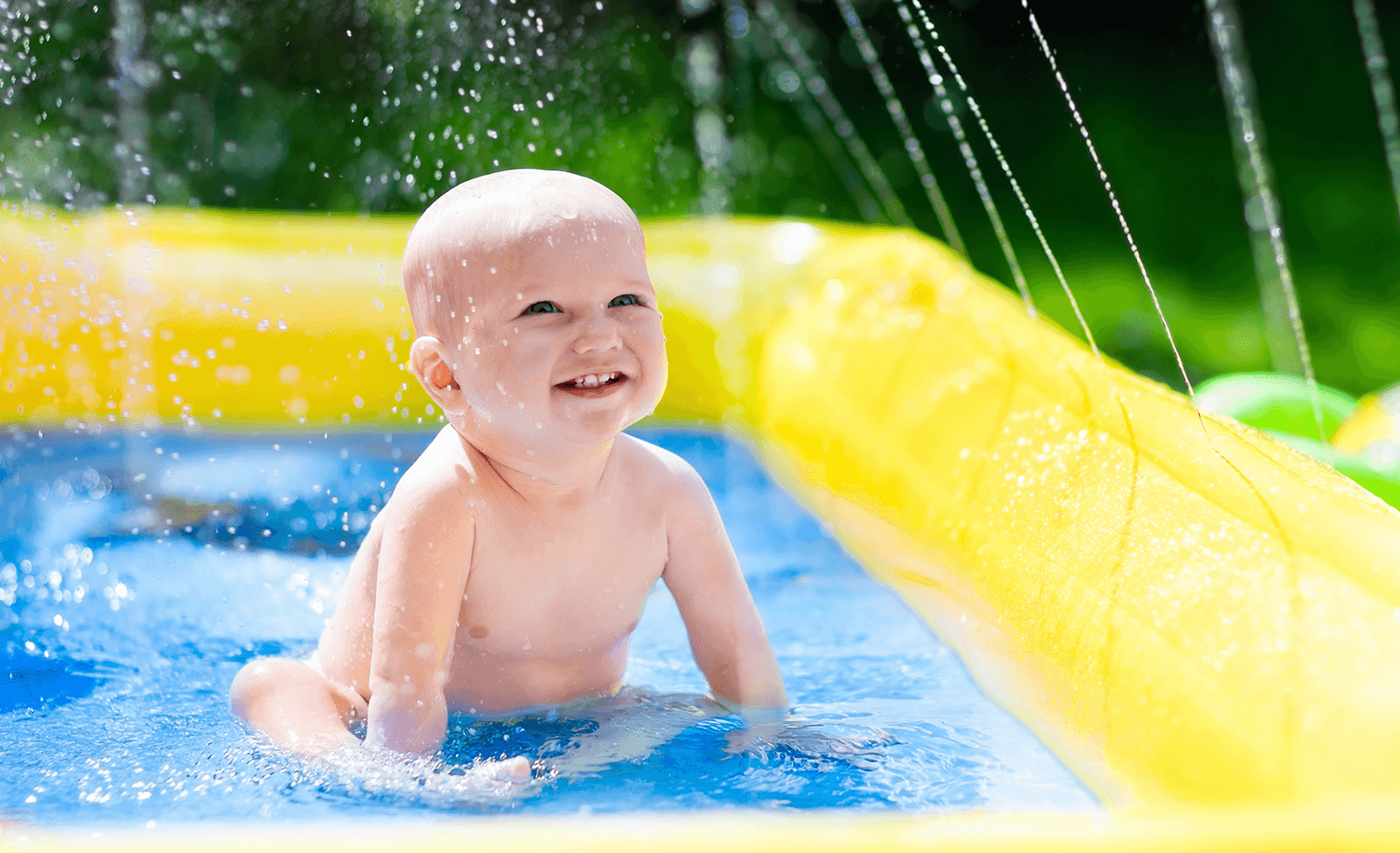 baby sitting in kid pool outside, smiling