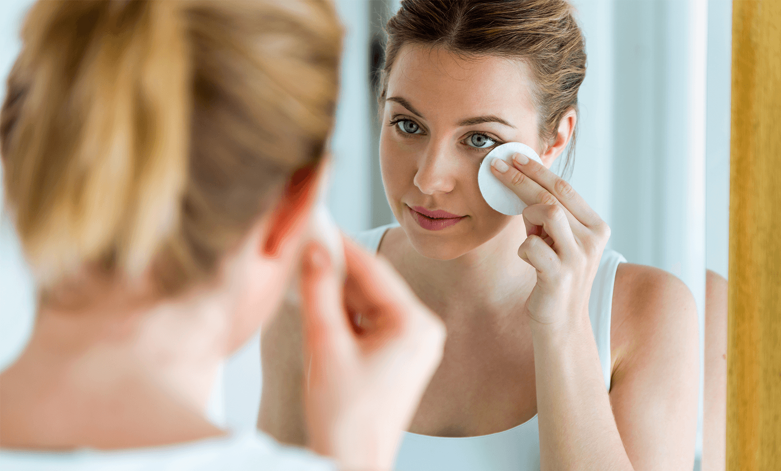 Woman applying a warm compress to her eye while looking in a mirror.