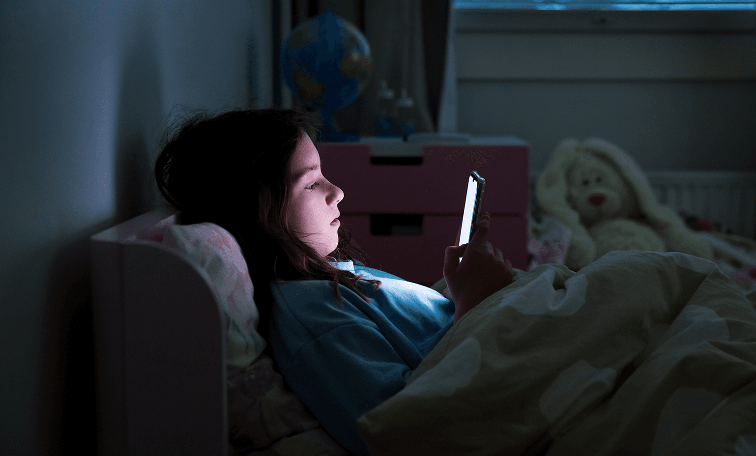 Teenager on their cellphone in bed at night.