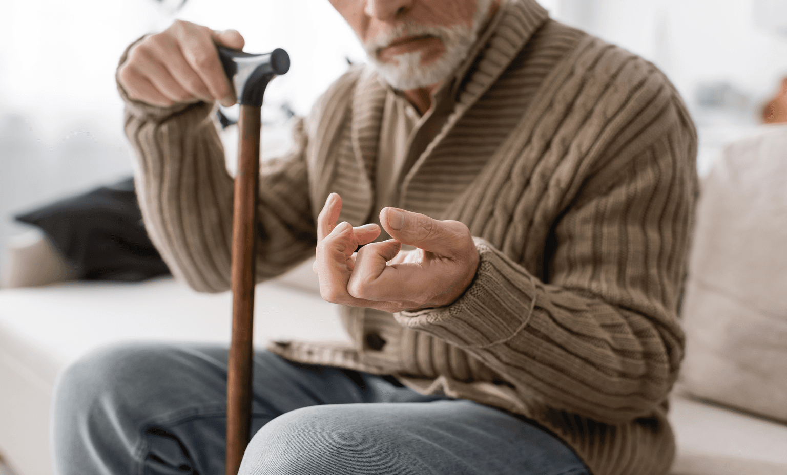 senior man with parkinson disease holding walking cane while sitting on couch