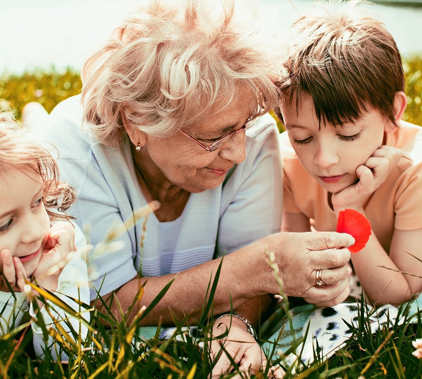 grandmother and grandkids sit in the grass and look at flowers