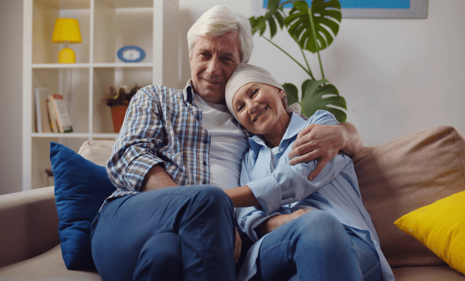 Smiling woman with cancer hugging husband sitting on couch at home.