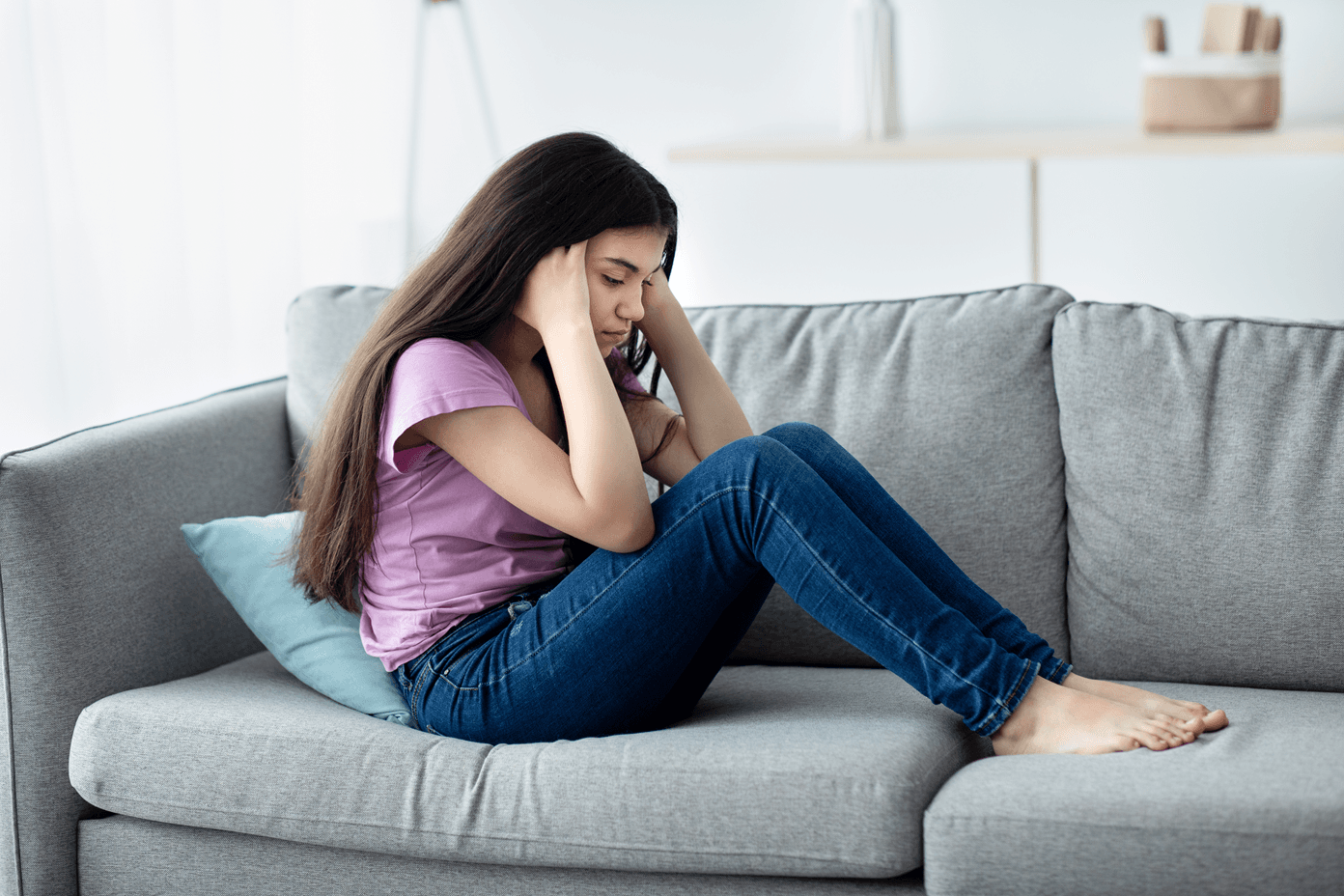 Unhappy teen girl holding her head, sitting on sofa at home,