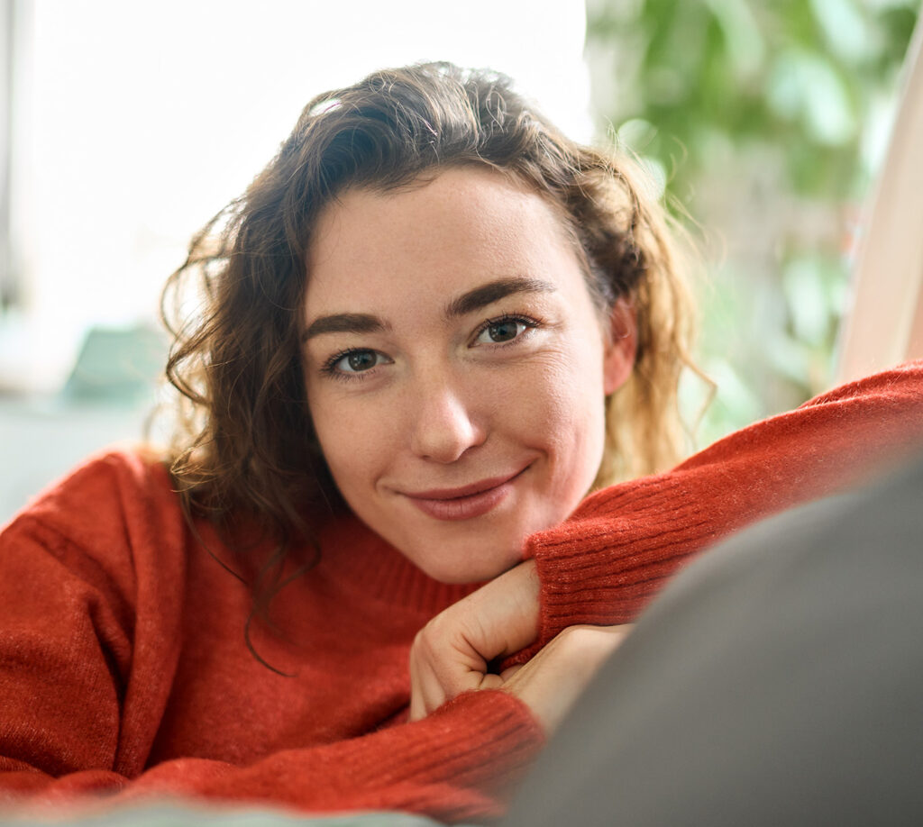 Woman with curly hair smiles while sitting on a couch