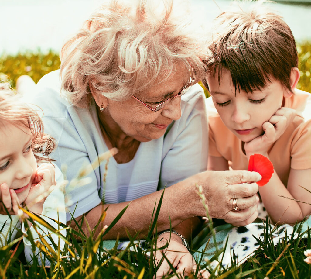 grandmother and grandkids sit in the grass and look at flowers