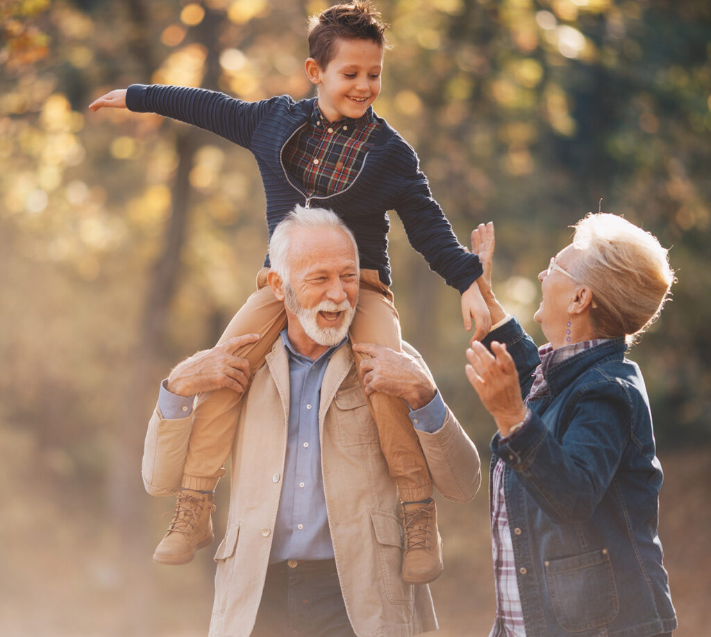 grandkid sits on grandfather's shoulders while on a walk outside with his grandma