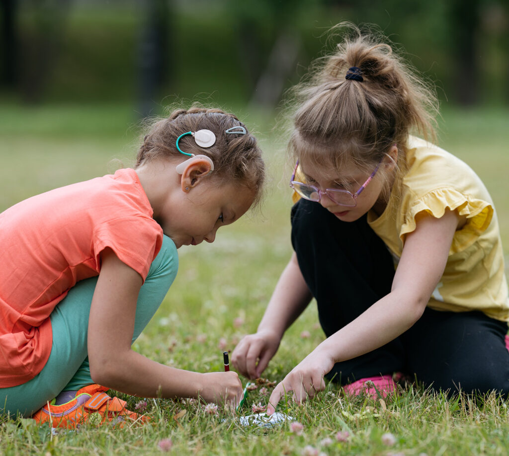 two young girls play outside and one wearings a hear device on her ear