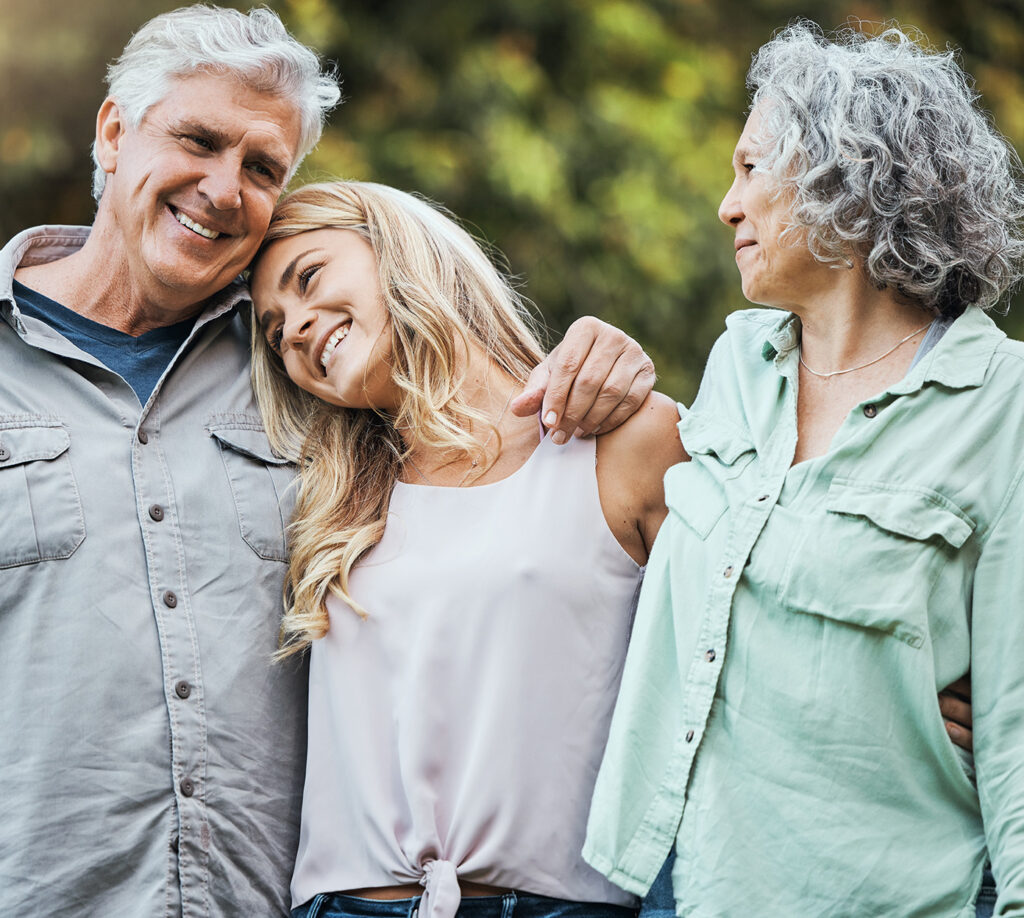 An adult child hug her mother and father while outside on a walk