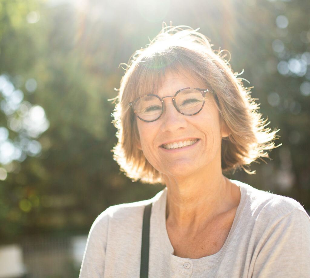 Older woman smiles outside while walking and the sun shines on her face
