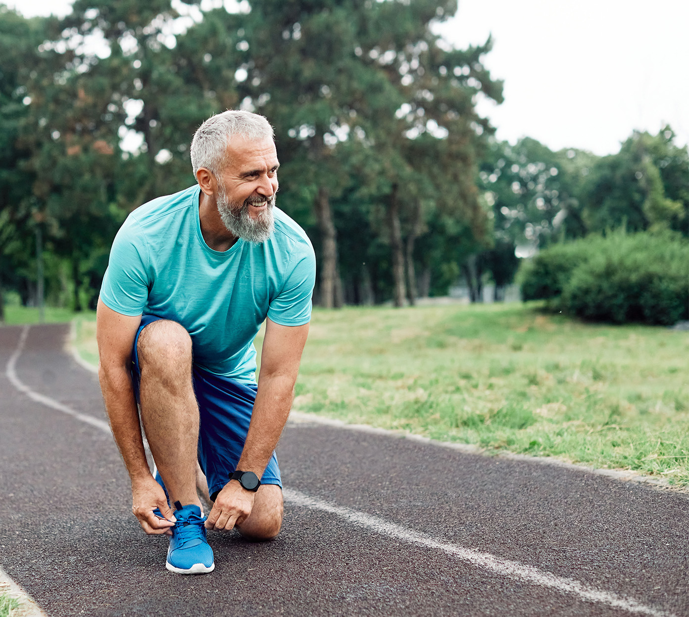 A man with grey hair kneels on a trail to tie his shoe