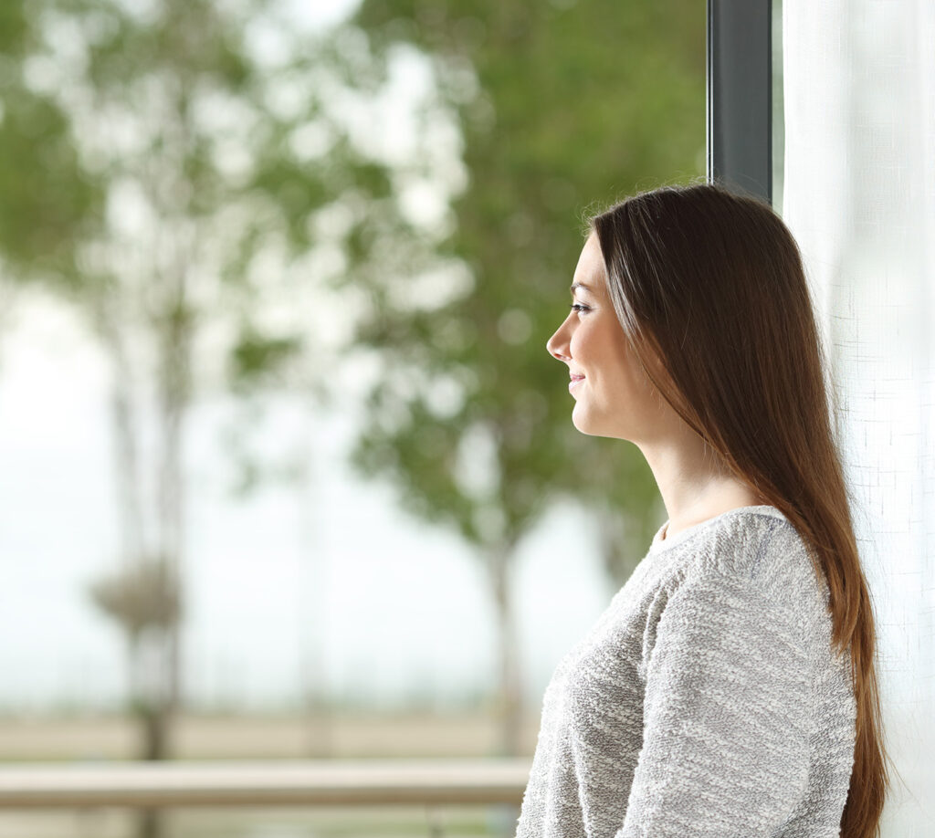 Woman looks at peace while looking out the window at trees