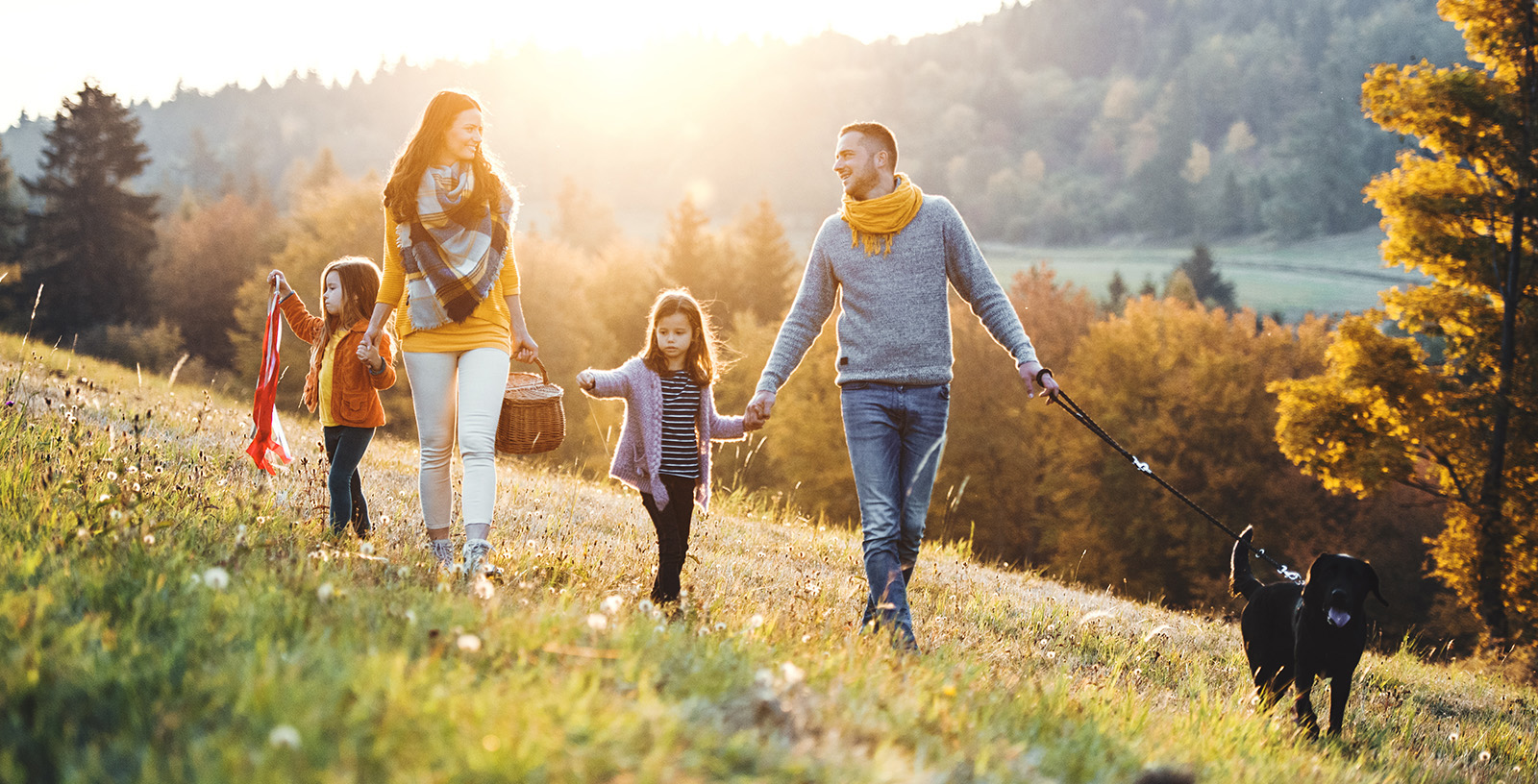 A young family walks a dog outside during the fall in the sun.