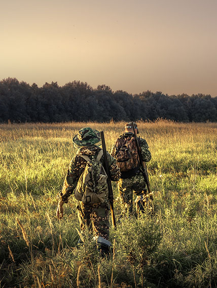 Two hunters in camouflage walk through a field