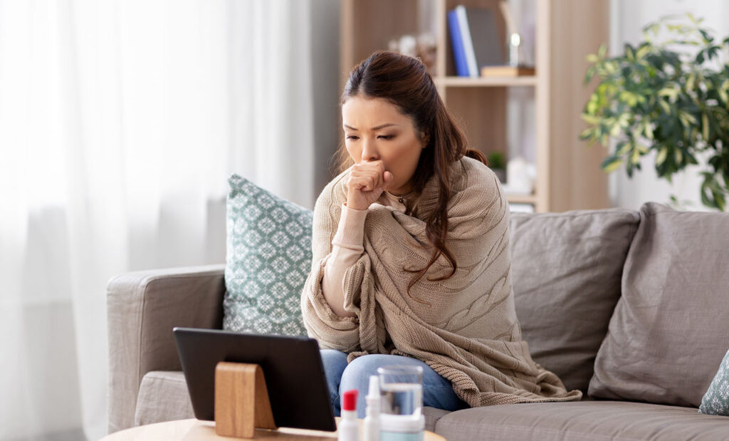 Woman with blanket wrapped around her sits in front of a tablet on a telehealth appointment