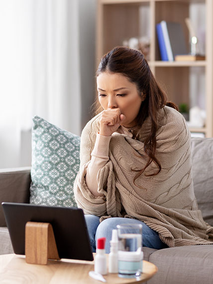 Woman with blanket wrapped around her sits in front of a tablet on a telehealth appointment