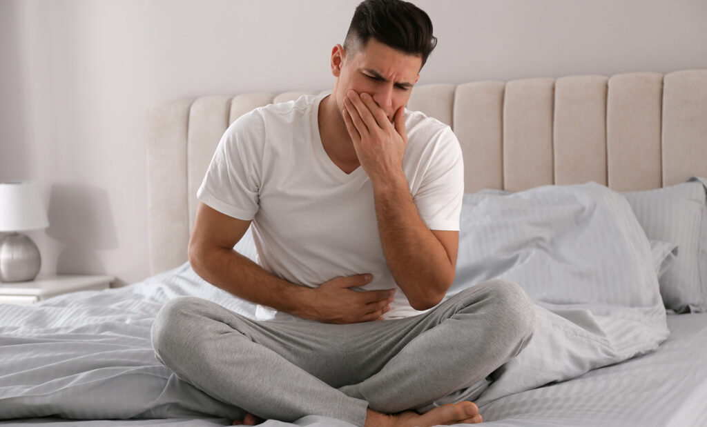 Man sits on bed with norovirus symptoms