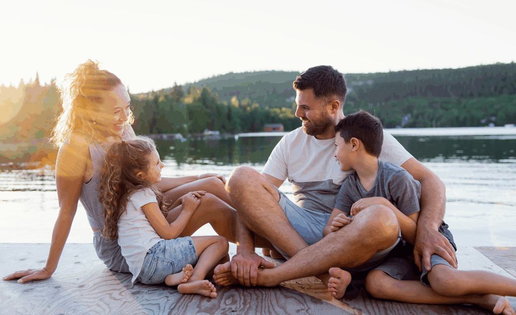 parents with two elementary aged kids sitting on dock at lake and smiling