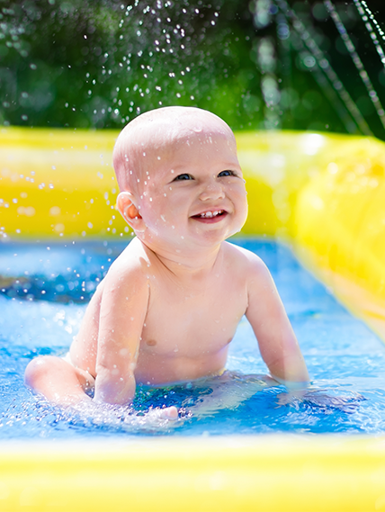 baby sitting in kid pool outside, smiling