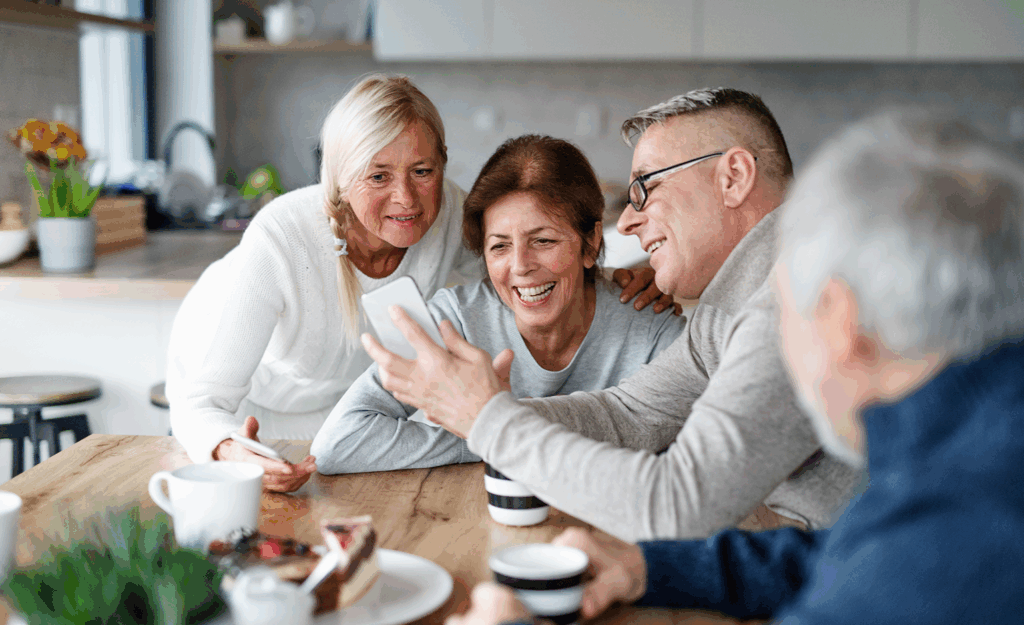 adult friends sitting around kitchen table, smiling and looking at someone's phone