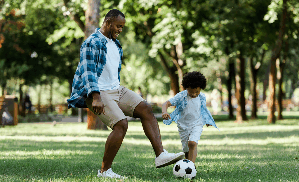 father and son playing soccer together in park