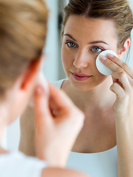 Woman applying a warm compress to her eye while looking in a mirror.