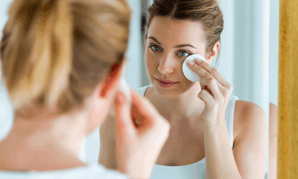 Woman applying a warm compress to her eye while looking in a mirror.