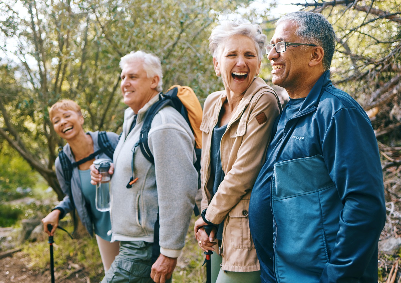 Four adults laughing together while hiking in the woods