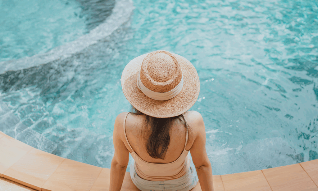 woman sitting facing pool wearing sunhat with feet in the pool