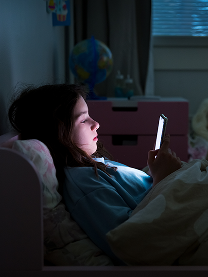 Teenager on their cellphone in bed at night.